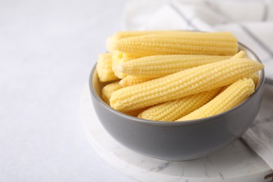 Photo of Tasty fresh yellow baby corns in bowl on white table, closeup. Space for text