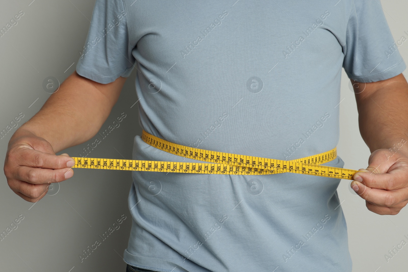 Photo of Man measuring waist with tape on grey background, closeup