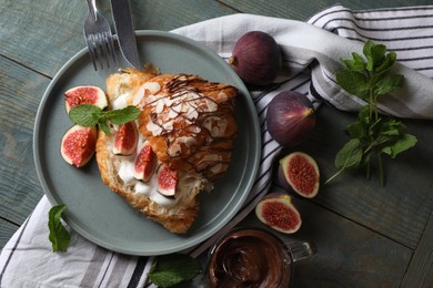 Delicious croissant with figs and cream served on light blue wooden table, flat lay