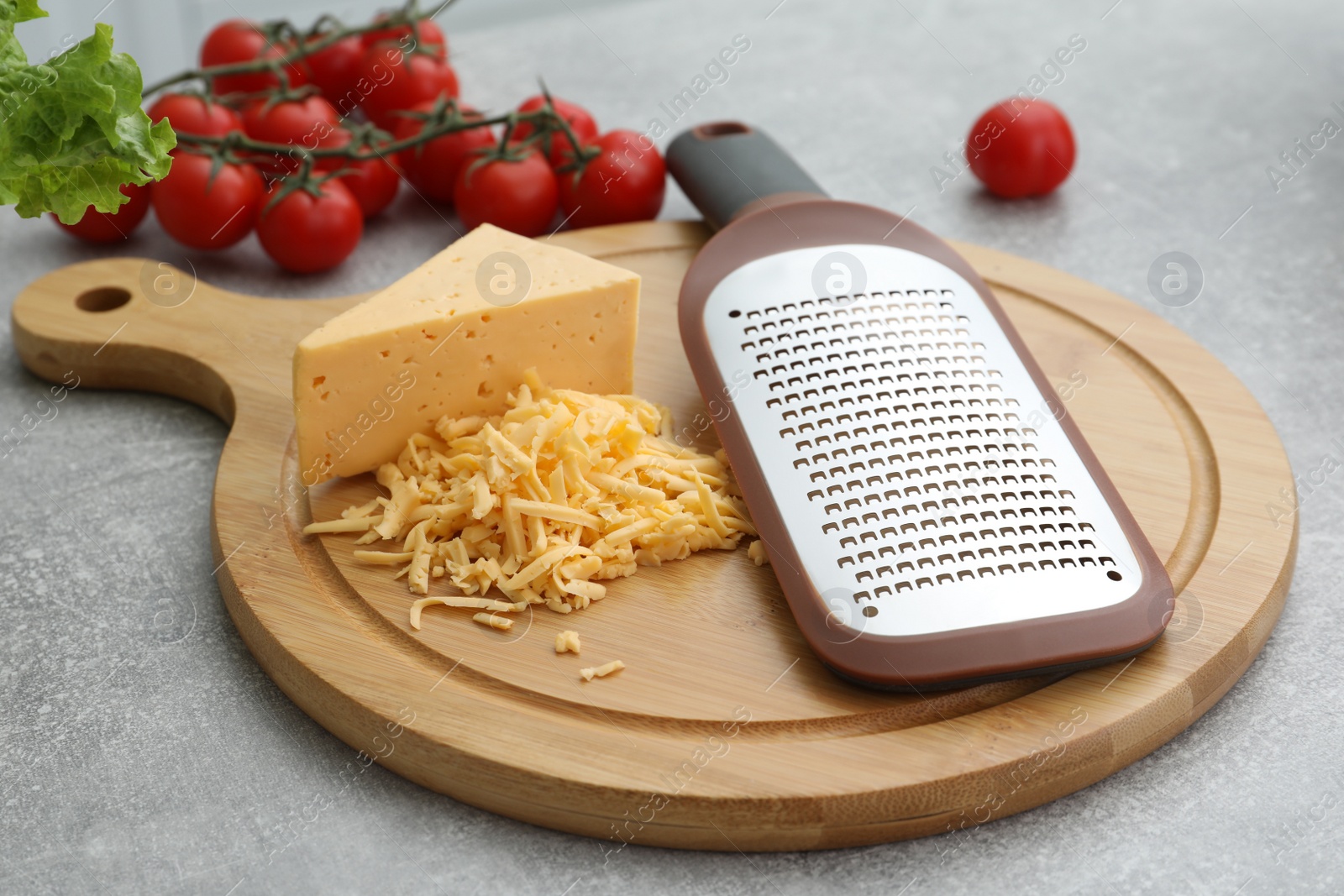 Photo of Wooden board with grater, cheese and vegetables on grey table