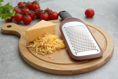 Photo of Wooden board with grater, cheese and vegetables on grey table