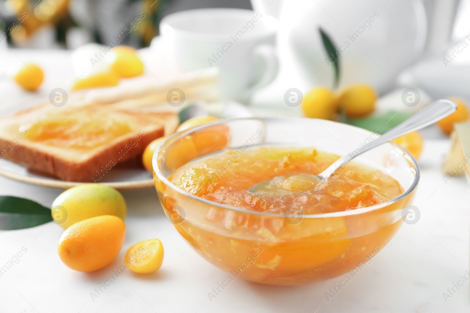 Photo of Delicious kumquat jam in glass bowl on white table, closeup