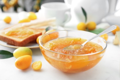 Delicious kumquat jam in glass bowl on white table, closeup