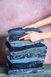 Photo of Woman folding stylish jeans on wooden table, closeup