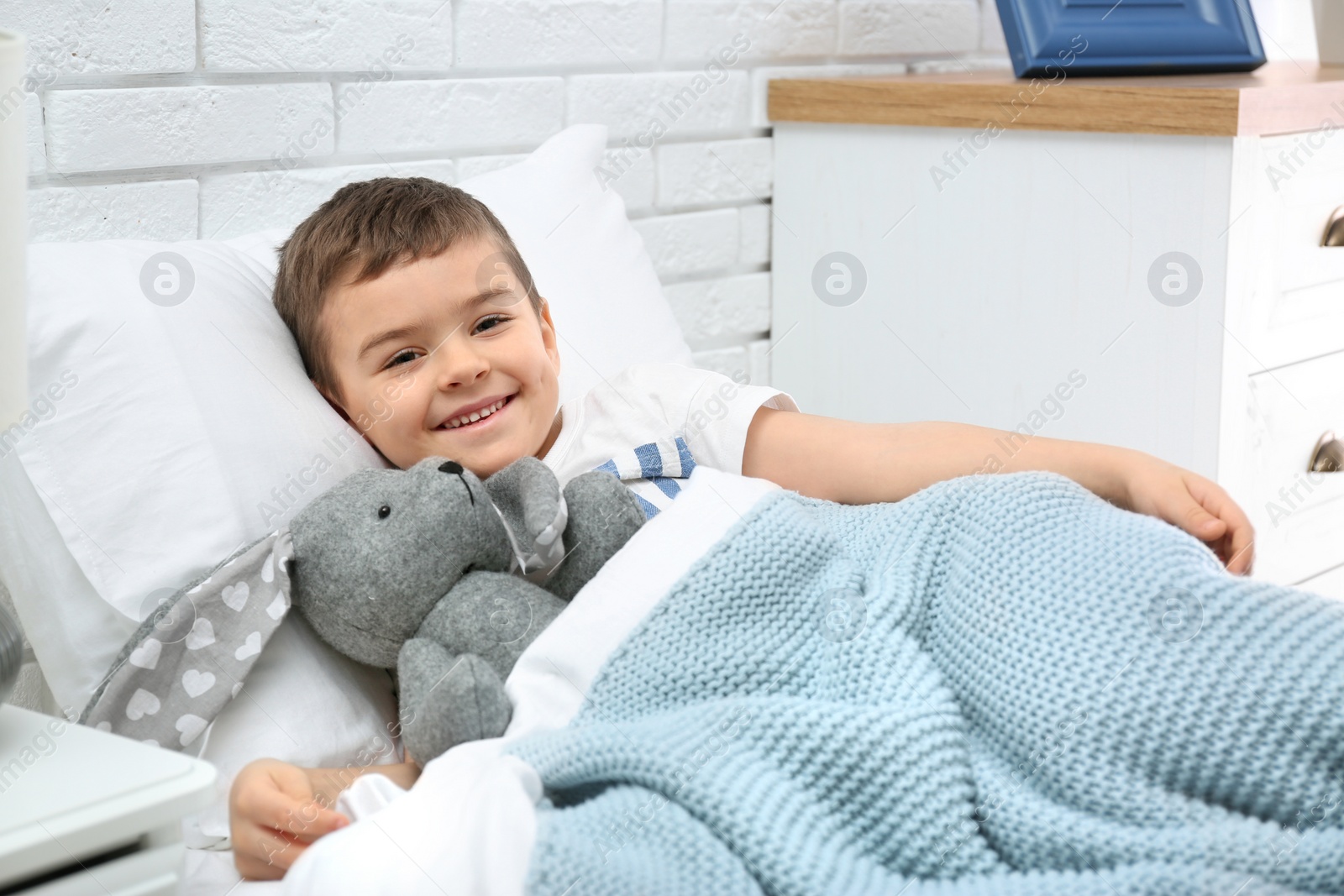 Photo of Cute child with stuffed bunny resting in bed at hospital