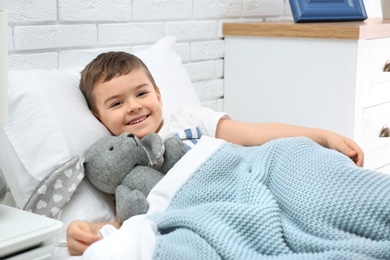 Cute child with stuffed bunny resting in bed at hospital