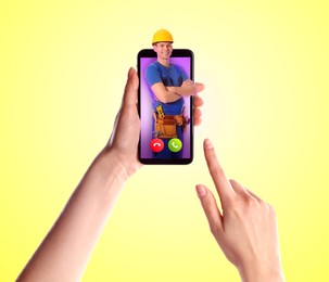 Woman with smartphone calling professional repairman on yellow background, closeup