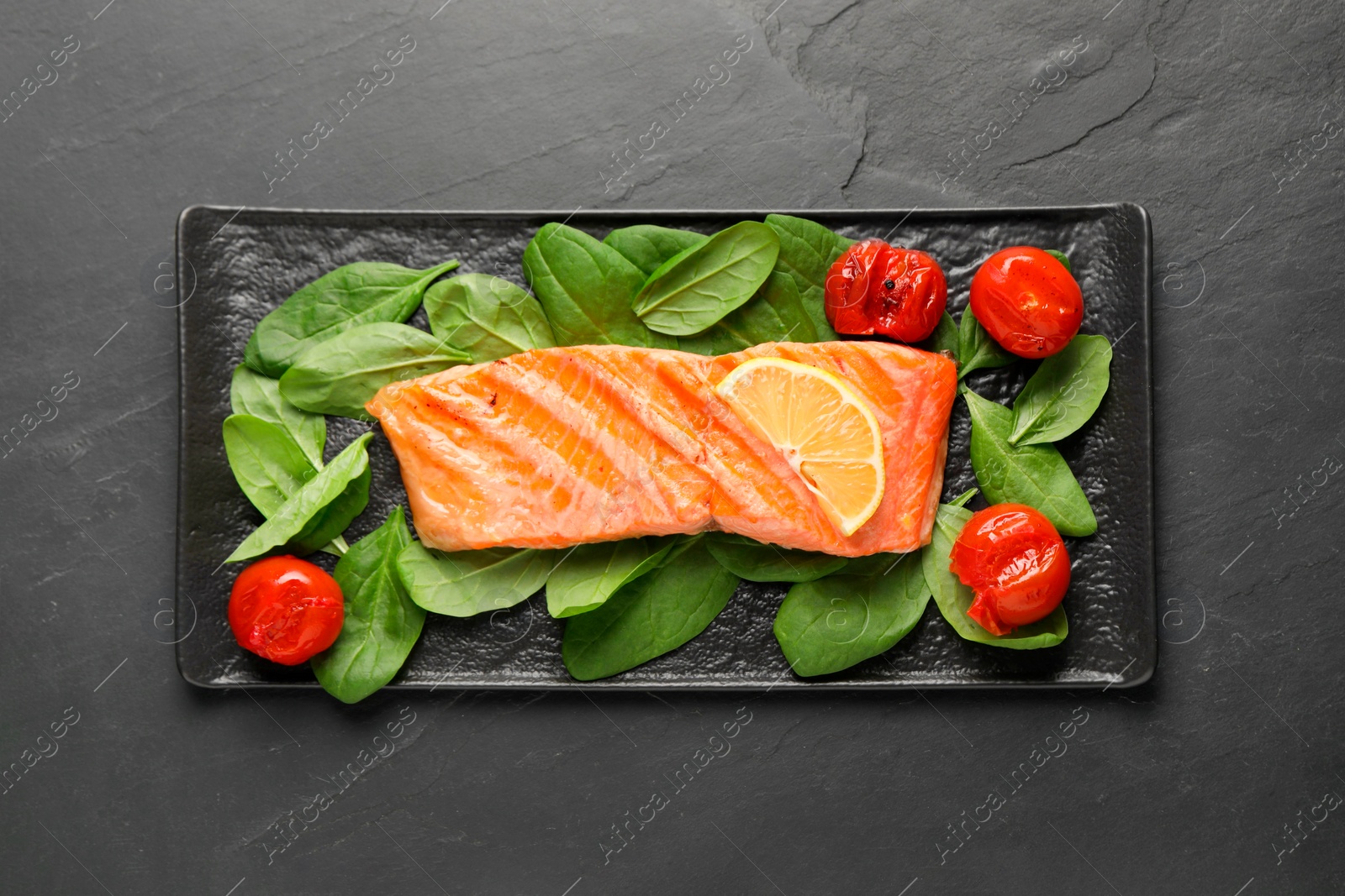 Photo of Tasty grilled salmon with tomatoes and spinach on black table, top view