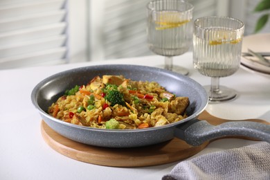 Photo of Tasty rice with meat and vegetables in frying pan on white table indoors