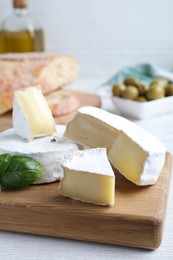 Tasty brie cheese with basil on white wooden table, closeup