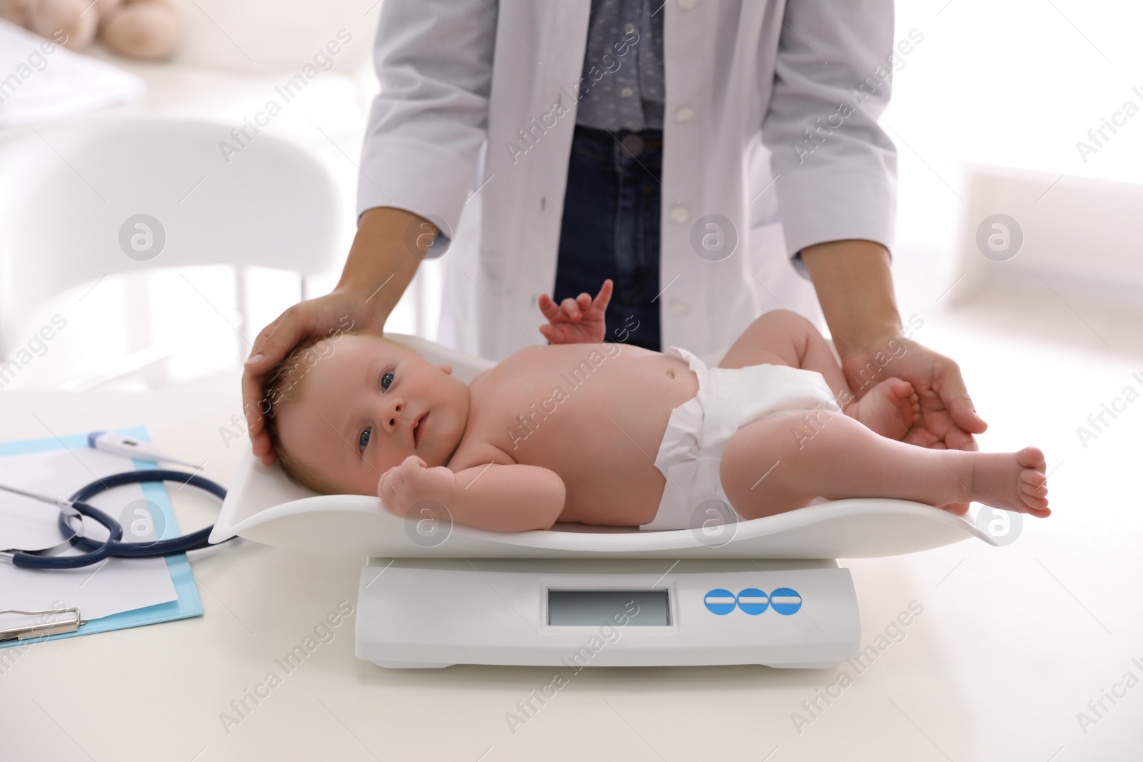 Photo of Doctor weighting cute baby in clinic, closeup. Health care