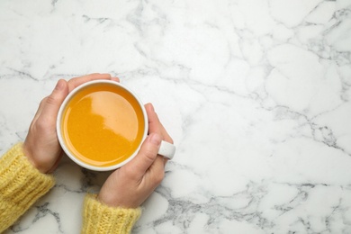 Woman holding cup with sea buckthorn tea at white table, top view. Space for text