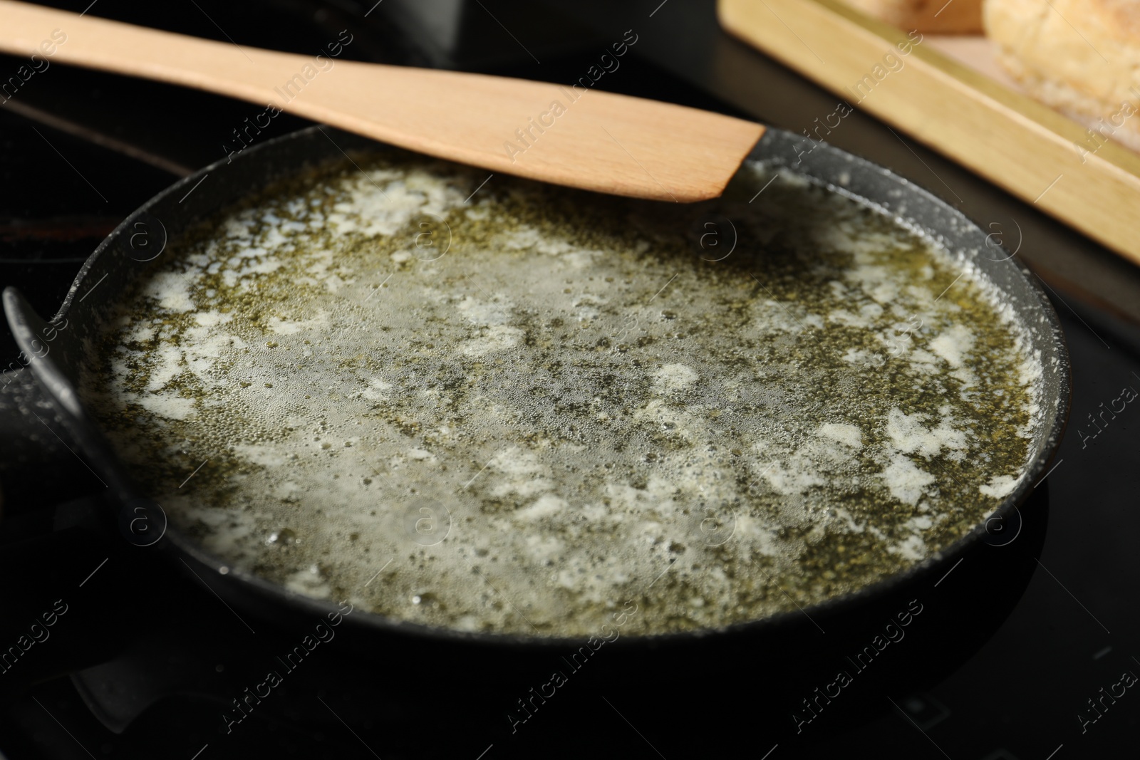 Photo of Melted butter in frying pan and wooden spatula on table, closeup