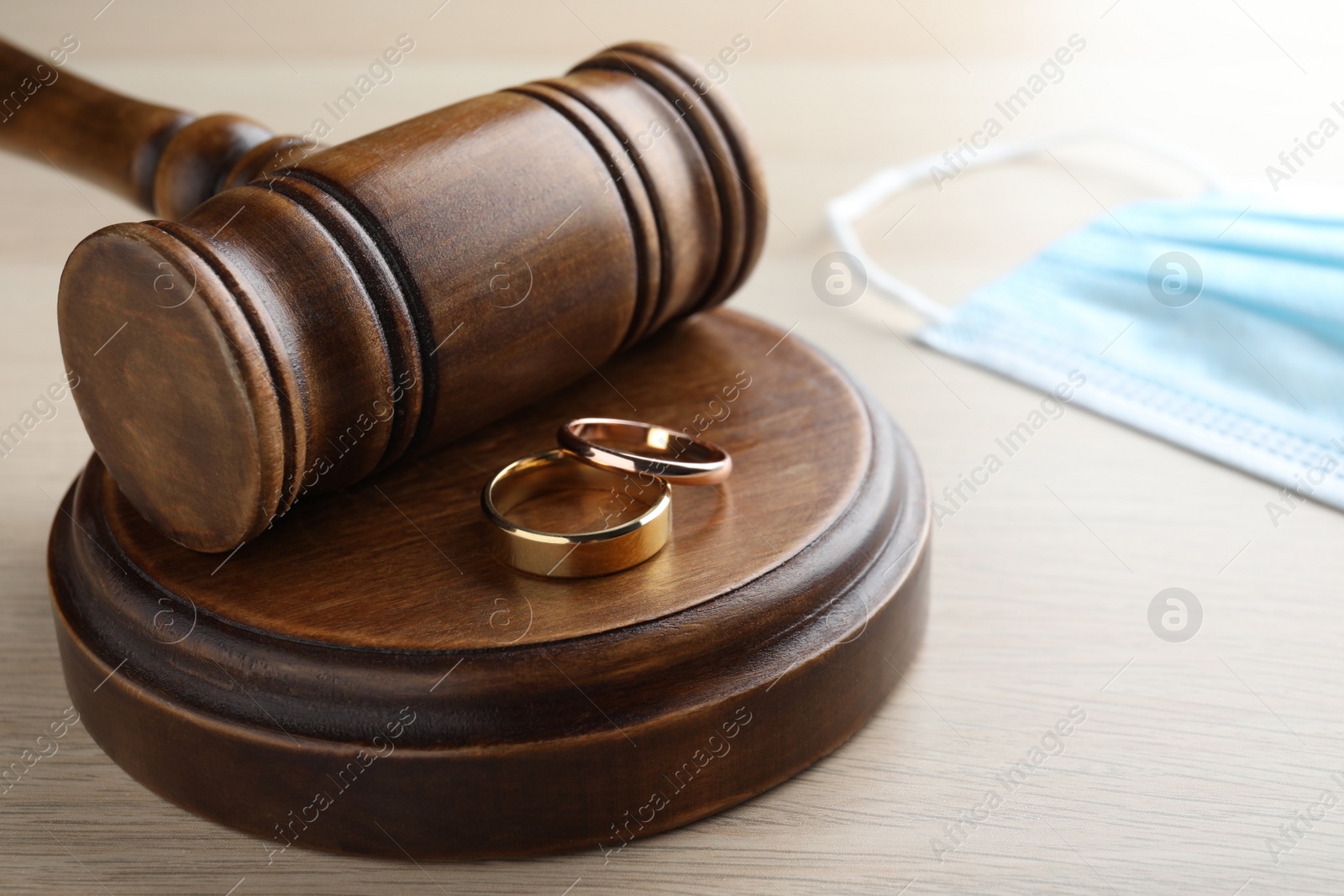 Photo of Gavel, wedding rings and protective mask on wooden table. Divorce during coronavirus quarantine
