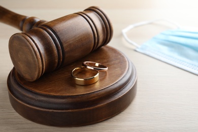Gavel, wedding rings and protective mask on wooden table. Divorce during coronavirus quarantine
