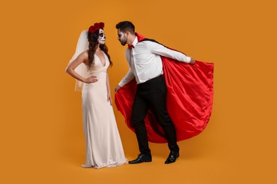 Photo of Couple in scary bride and vampire costumes on orange background. Halloween celebration