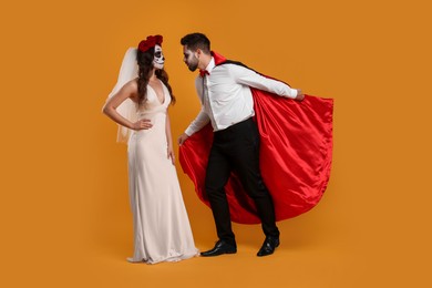 Couple in scary bride and vampire costumes on orange background. Halloween celebration