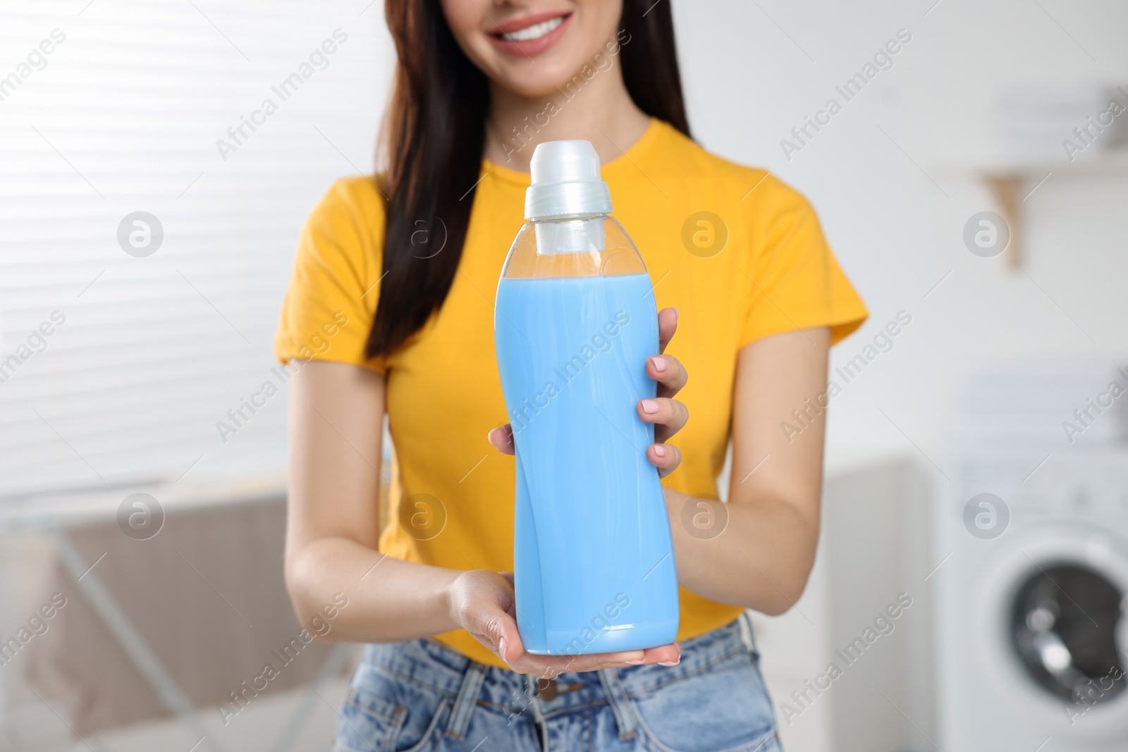 Photo of Woman holding fabric softener in bathroom, closeup. Space for text