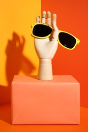 Photo of Wooden mannequin hand with stylish sunglasses on color background