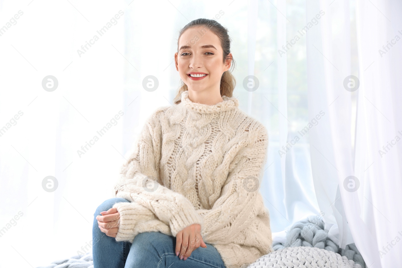 Photo of Beautiful teenage girl in warm cozy sweater sitting near window at home