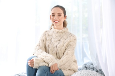 Beautiful teenage girl in warm cozy sweater sitting near window at home