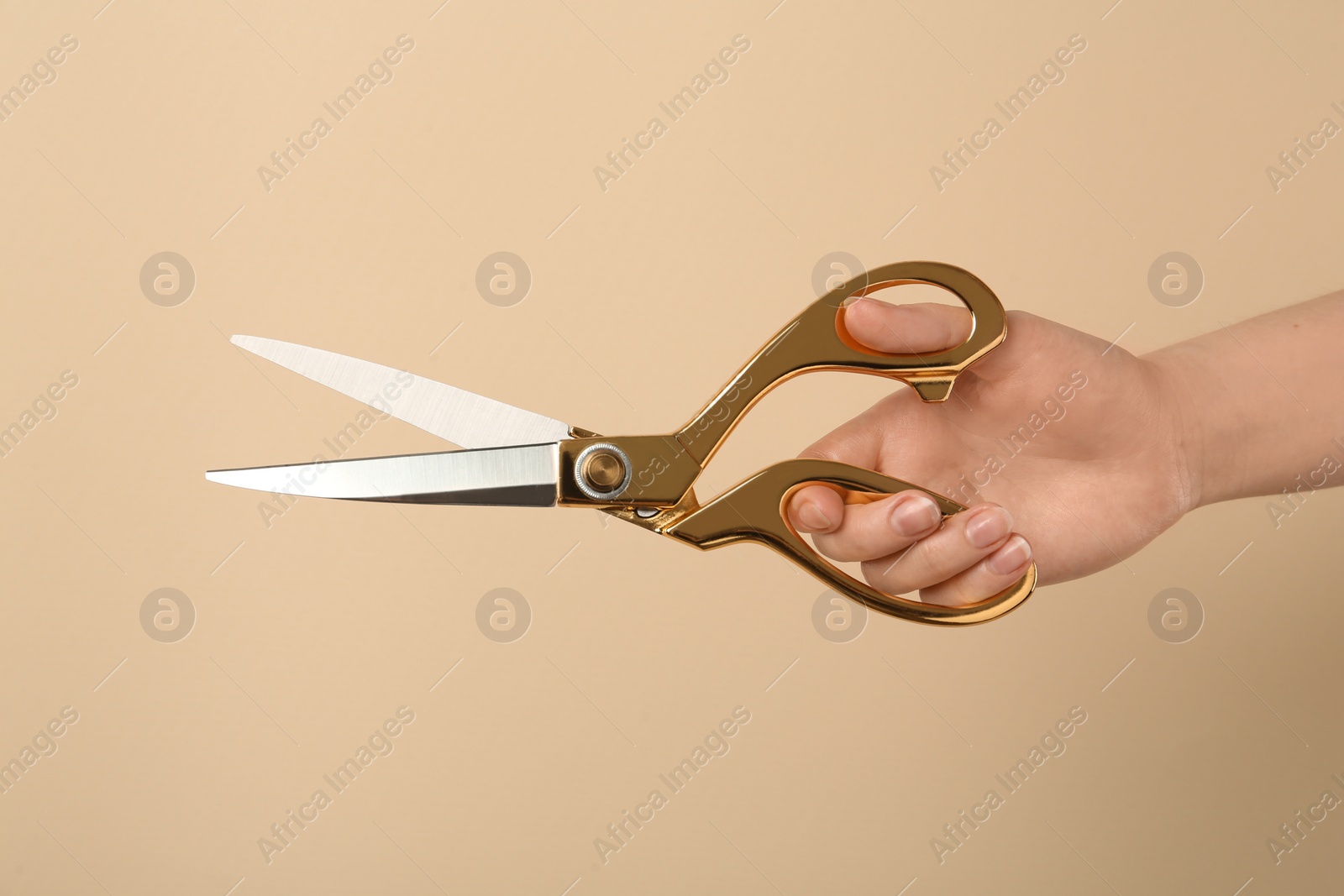 Photo of Woman holding sewing scissors on beige background, closeup