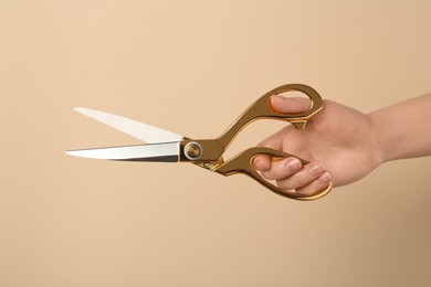 Photo of Woman holding sewing scissors on beige background, closeup