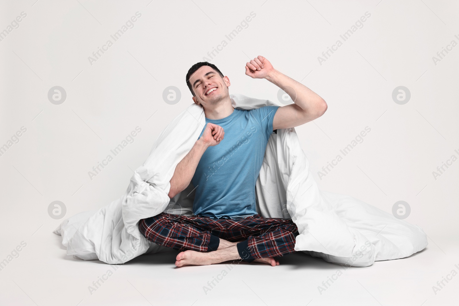 Photo of Happy man in pyjama wrapped in blanket on light grey background