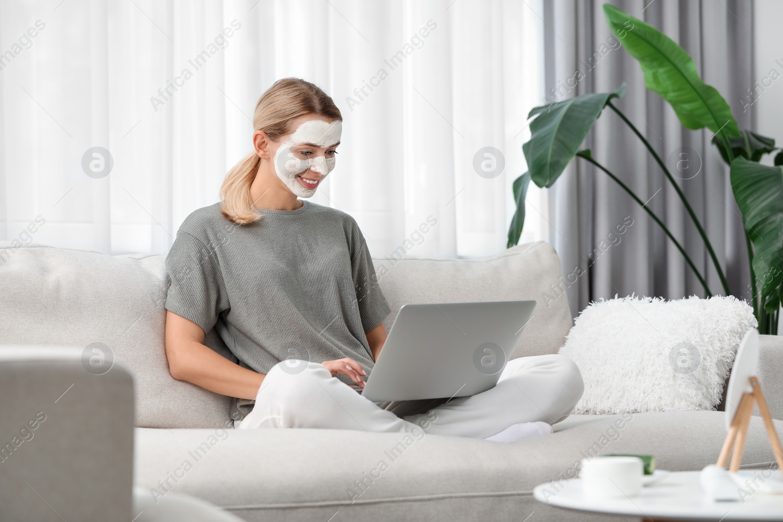 Photo of Young woman with face mask using laptop on sofa at home. Spa treatments