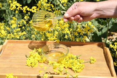 Man pouring rapeseed oil from jug into bowl at tray outdoors, closeup