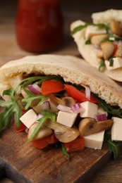 Photo of Delicious pita sandwiches with cheese, mushrooms, tomatoes and arugula on wooden table, closeup