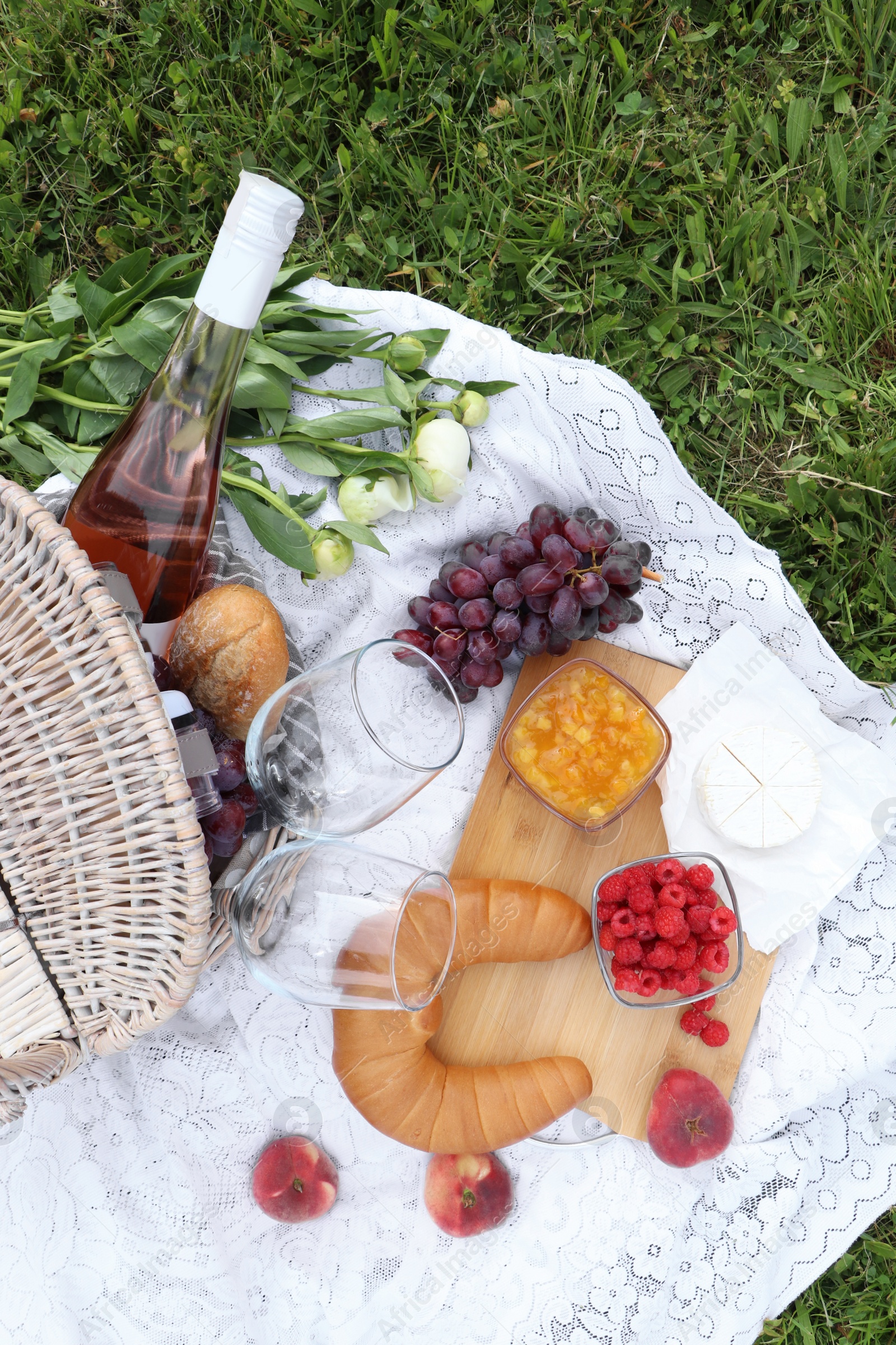 Photo of Picnic blanket with tasty food, flowers and cider on grass outdoors, flat lay