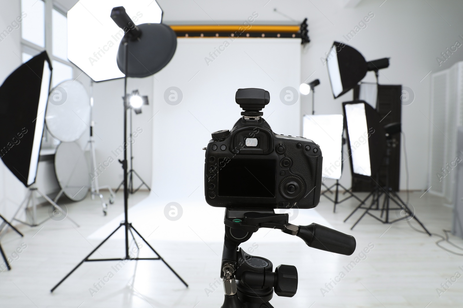 Photo of Tripod with camera and professional lighting equipment in modern photo studio