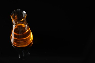 Photo of Glass flask with yellow oil on black background, space for text