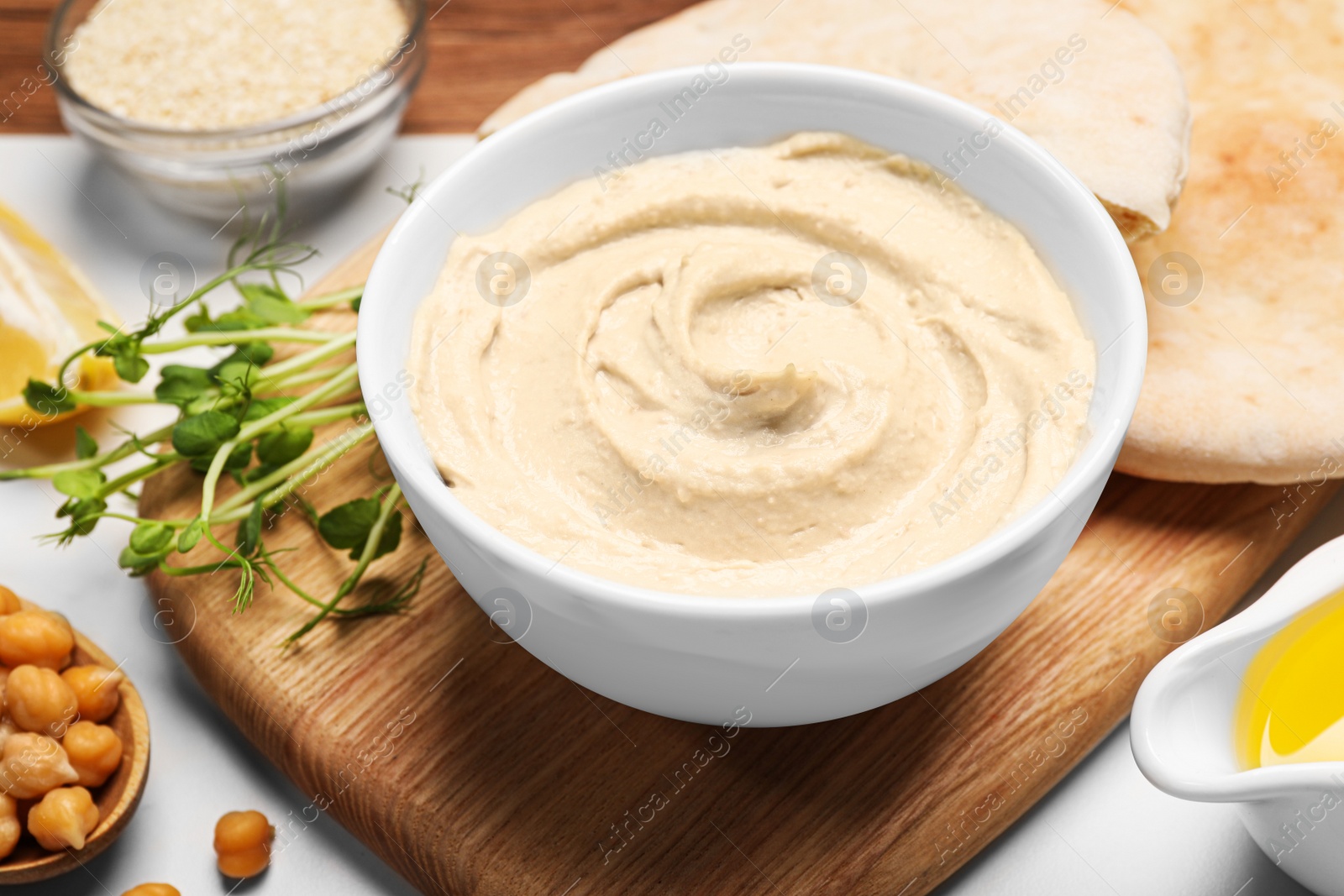 Photo of Delicious hummus and different ingredients on white table