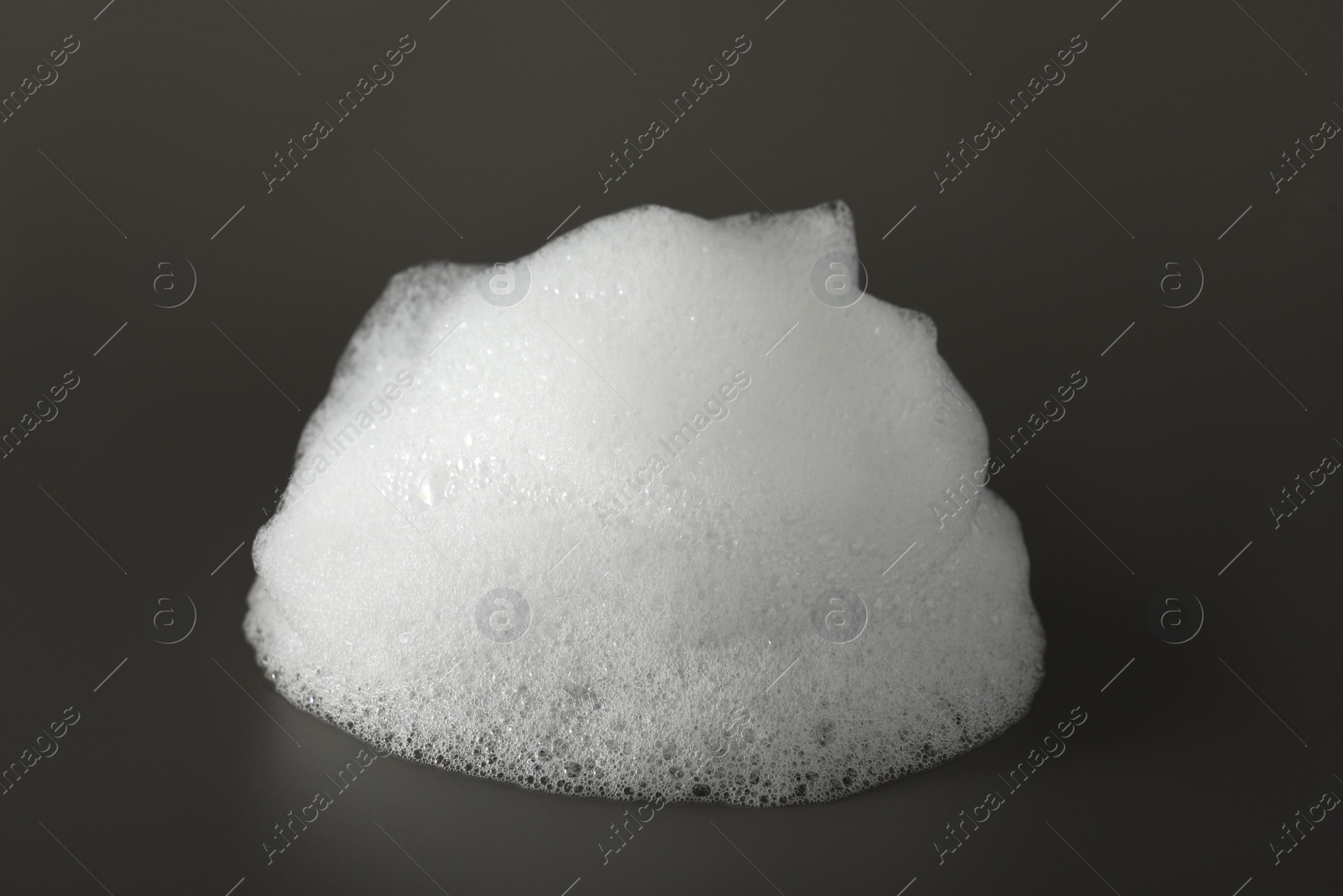 Photo of Drop of fluffy bath foam on grey background, closeup