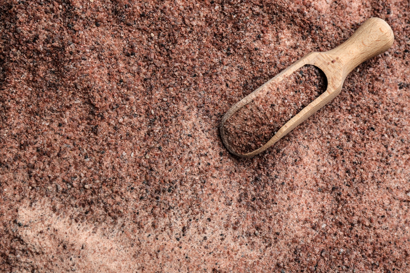 Photo of Pile of ground black salt with wooden scoop, top view