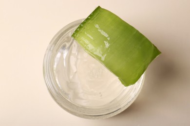 Jar of natural gel and cut aloe on beige background, top view