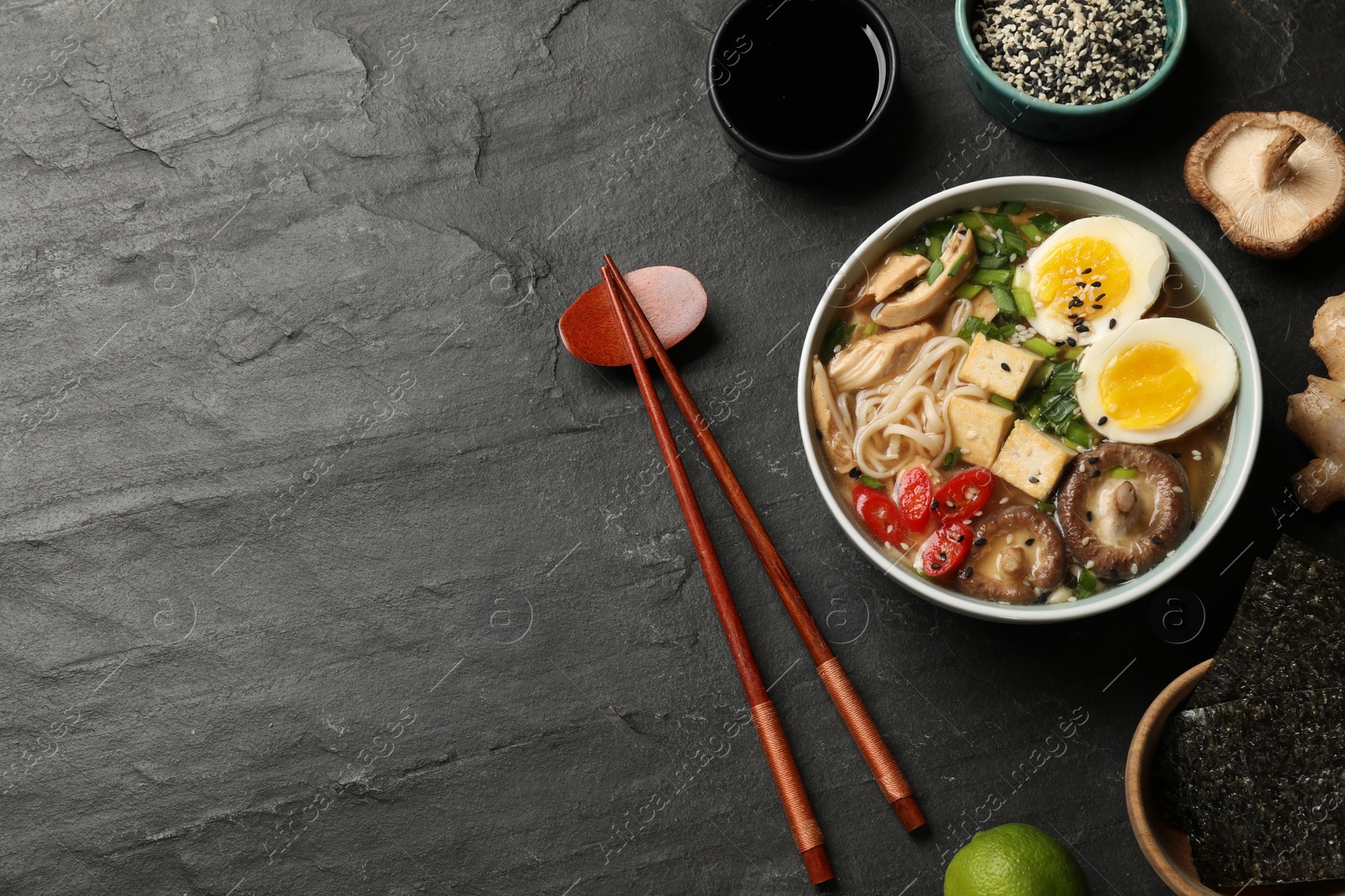 Photo of Noodle soup. Bowl of delicious ramen, ingredients and chopsticks on black table, flat lay. Space for text