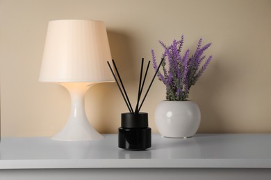 Aromatic reed air freshener, lamp and lavender flowers on white table indoors