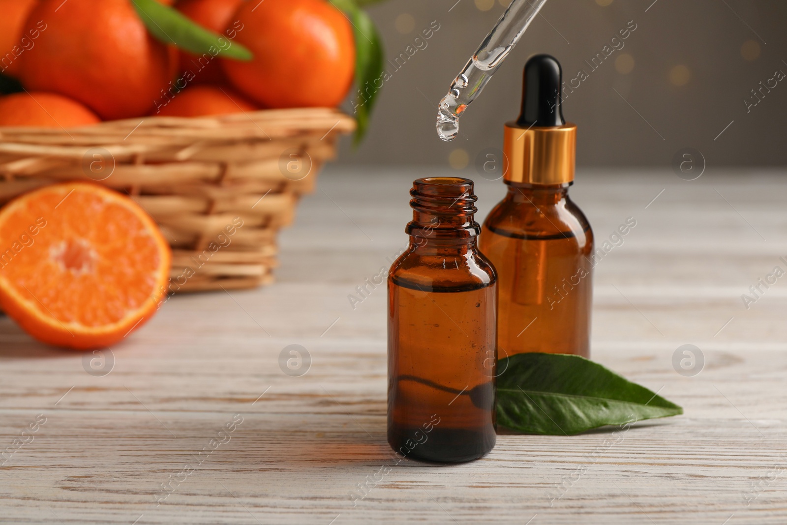 Photo of Tangerine essential oil dripping from pipette into bottle on wooden table