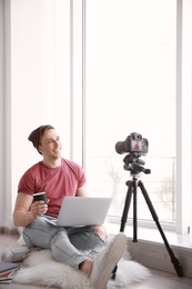 Young blogger with laptop recording video near window