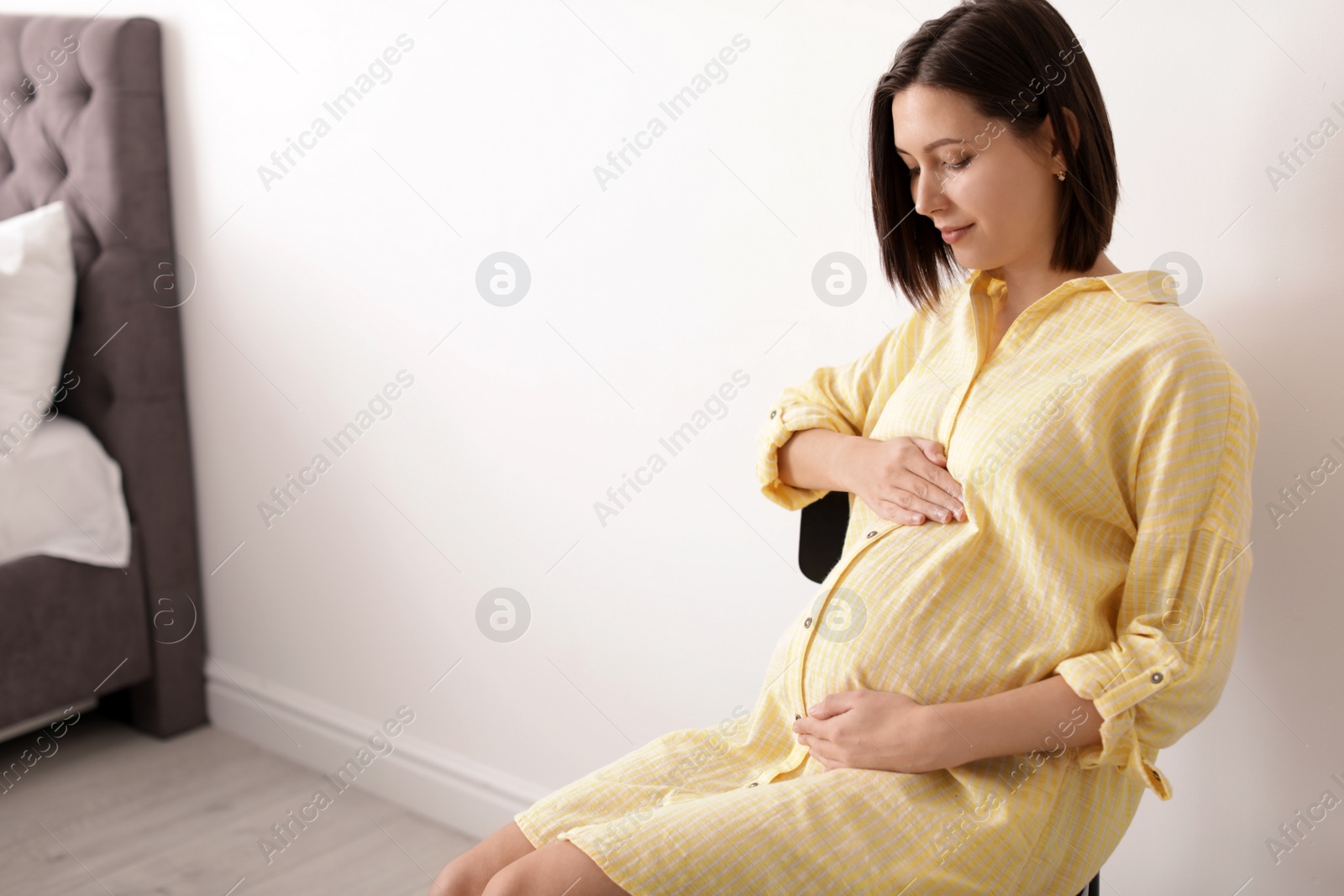 Photo of Beautiful pregnant woman sitting in light room. Space for text