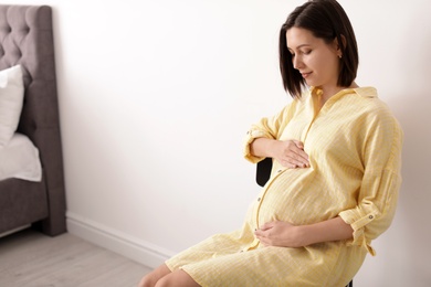 Beautiful pregnant woman sitting in light room. Space for text