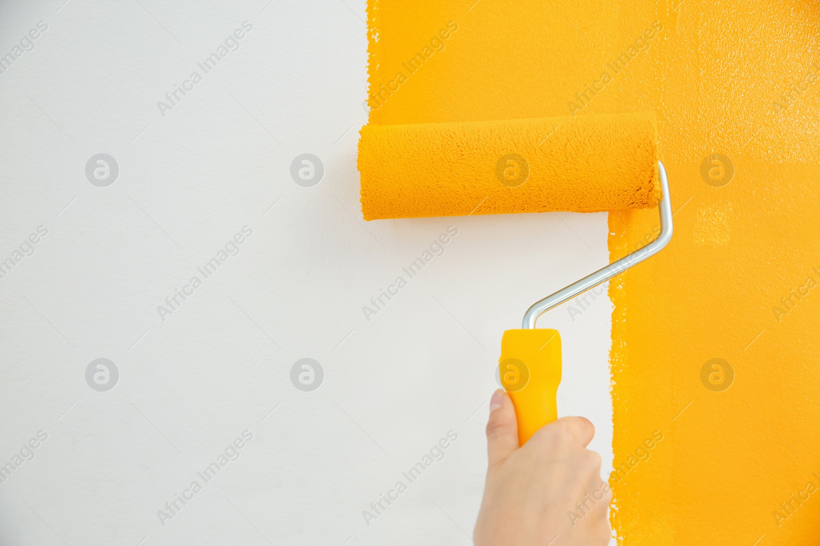 Photo of Woman painting white wall with yellow dye, closeup. Interior renovation