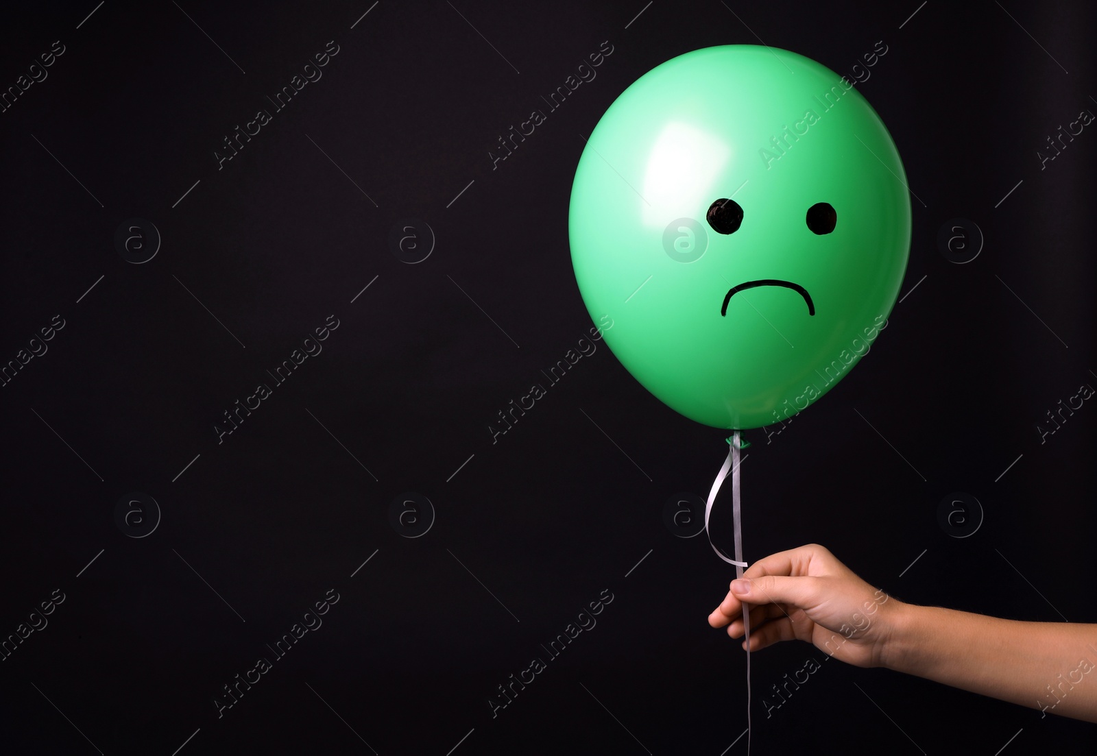 Photo of Woman holding balloon with sad face on black background, space for text. Threat of depression