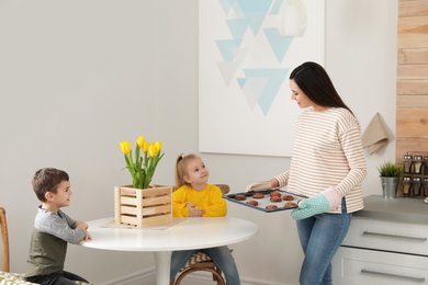 Photo of Mother treating kids with oven baked cookies indoors