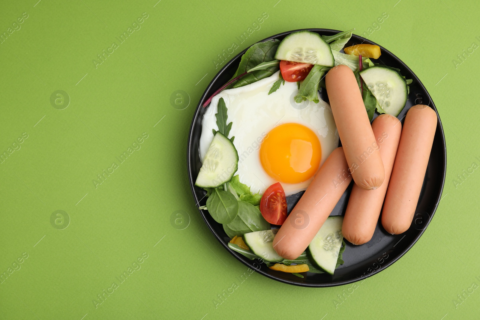 Photo of Delicious breakfast with boiled sausages and fried egg on green background, top view. Space for text