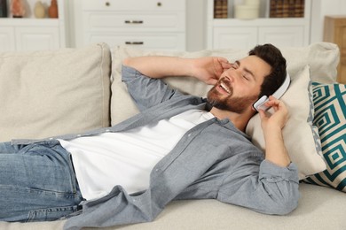 Photo of Happy man listening music with headphones on sofa indoors