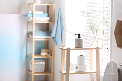 Photo of Soap dispenser and toilet paper on wooden stand in bathroom